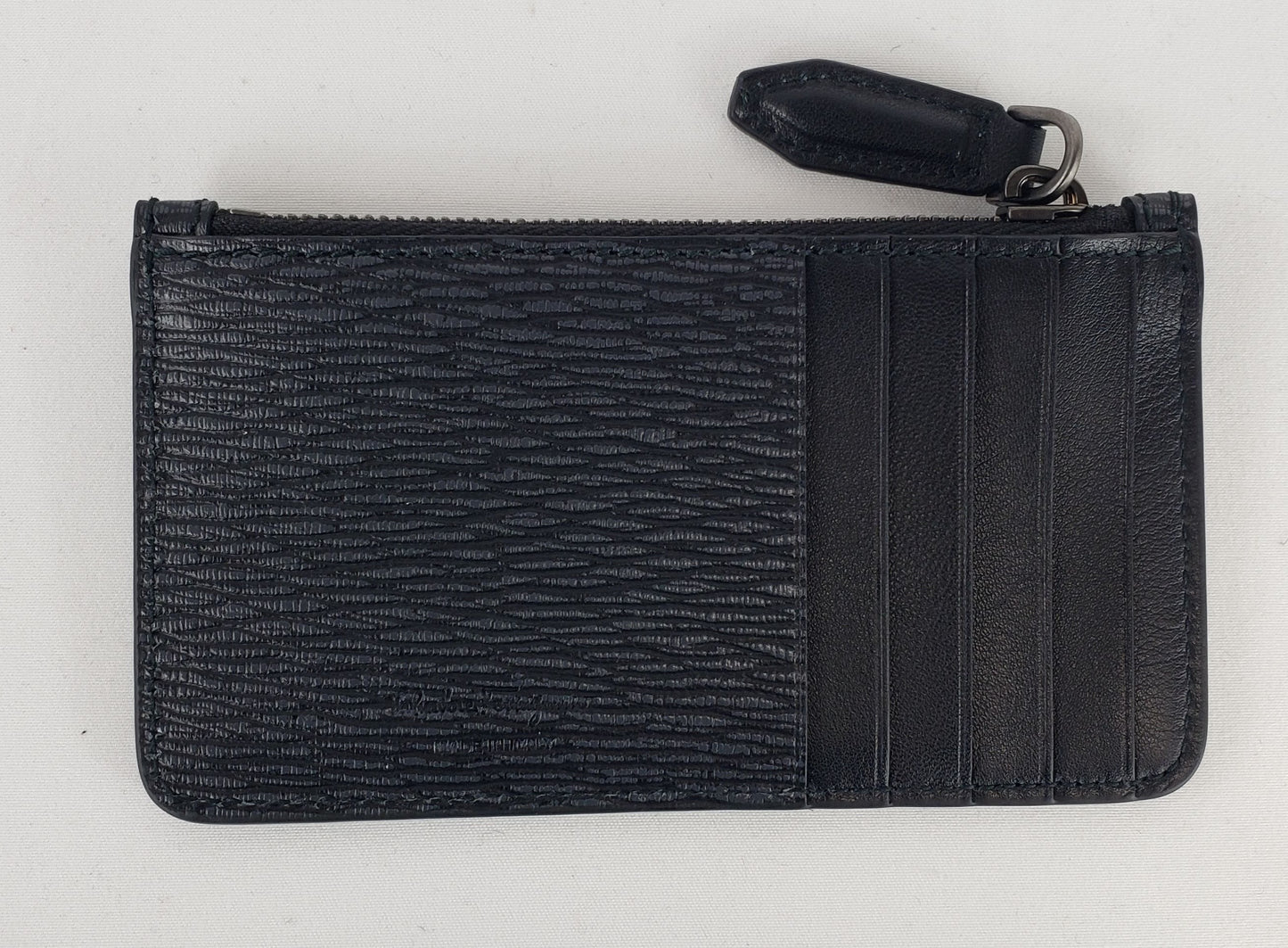 Black card holder Dark silver-toned hardware featuring Ferragamo name accent 100% pebbled leather 1 zipped pouch and 5 card slots 5.25" x 2.75" x 0.5" Product number 0670661 Made in Italy