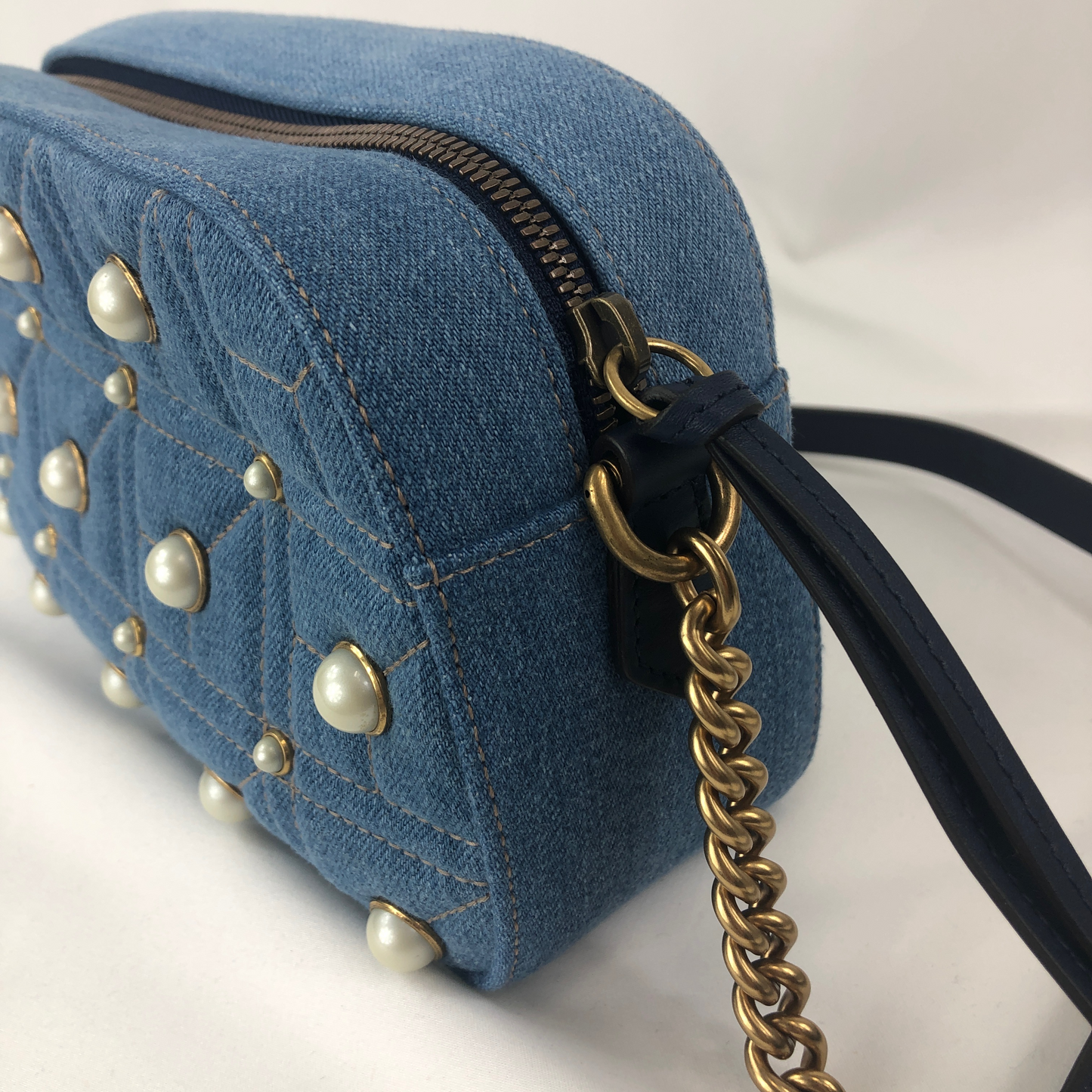 The Gucci Marmont Pearl Crossbody Bag in Denim is a modern take on a classic look. Light wash Matelassé denim Gucci Small GG Marmont Pearl Shoulder Bag with gold-tone hardware, single flat shoulder strap with chain-link accents, creme contrast stitching throughout, Running GG adornment at front face, pearl embellishments throughout exterior, coral satin interior lining, single interior slit pocket and zip closure at top. Includes dust bag. Authentic and rare handbags from Gavriel.us