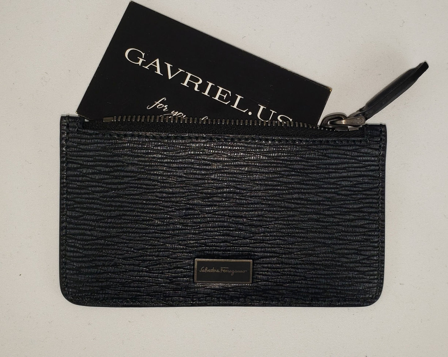 Extravagance in its simplest form, this Ferragamo card holder brings us back to basics in a timeless way. For a small wallet that you can slip into your pocket for easy access, this slim design is ideal for all situations! Equipped with a zipped pouch to keep coins and bills along with 5 card slots, you can safely carry all your necessities in a compact design. This wallet is made of durable pebbled leather and dawns a dark, signature Ferragamo logo accent. 