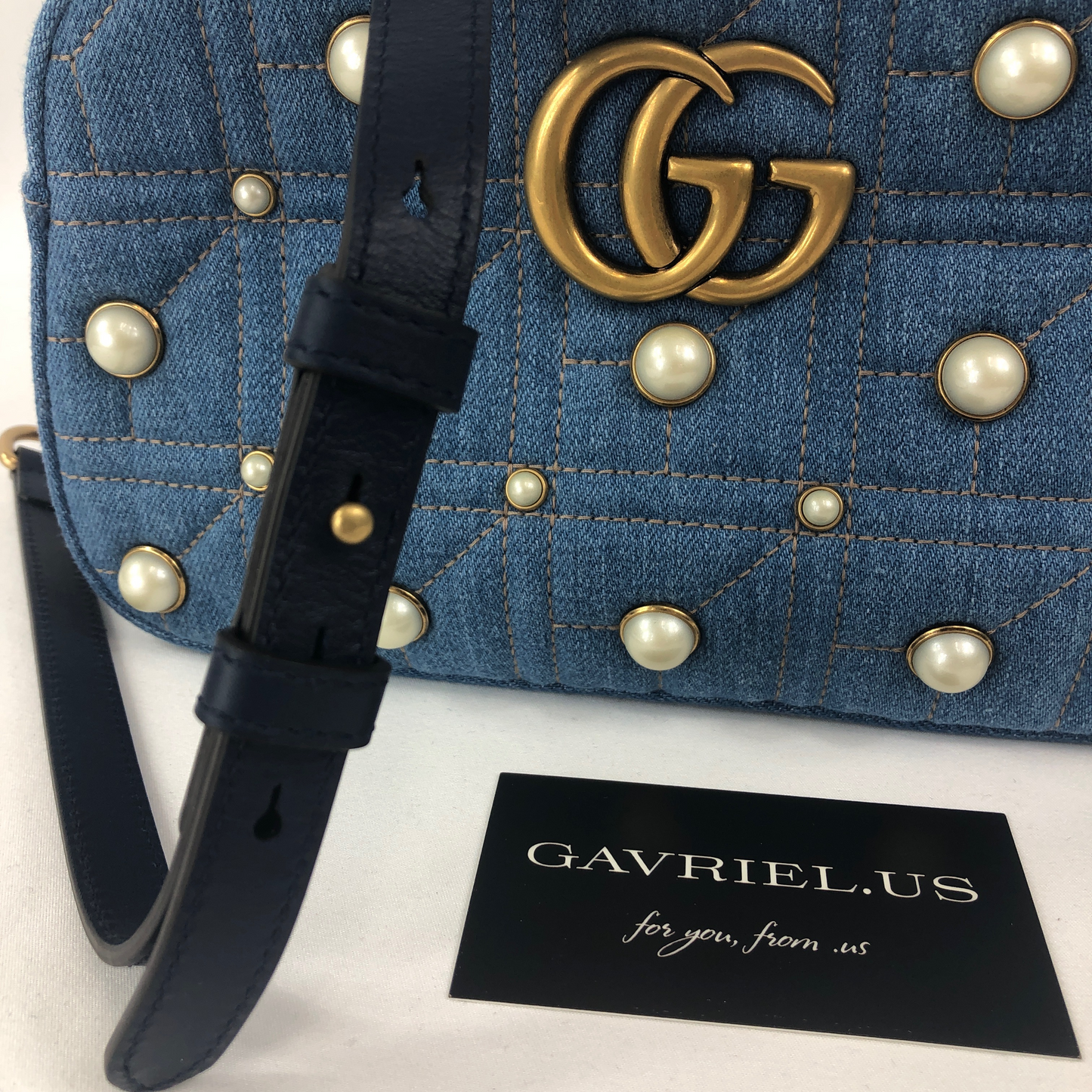 The Gucci Marmont Pearl Crossbody Bag in Denim is a modern take on a classic look. Light wash Matelassé denim Gucci Small GG Marmont Pearl Shoulder Bag with gold-tone hardware, single flat shoulder strap with chain-link accents, creme contrast stitching throughout, Running GG adornment at front face, pearl embellishments throughout exterior, coral satin interior lining, single interior slit pocket and zip closure at top. Includes dust bag. Authentic and rare handbags from Gavriel.us