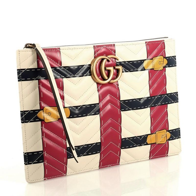 The Gucci Matelasse Trompe L'Oeil Print GG Marmont Pouch in White is crafted of lovely textured calfskin leather in black. This bag features chevron stitching, an aged gold interlocking GG logo and a beige fabric interior. The pattern is designed into woven navy and red stripes with print buckles. The term "trompe l'oeil" is French for a visual illusion in art, especially as used to trick the eye into perceiving a painted detail as a three-dimensional object. 