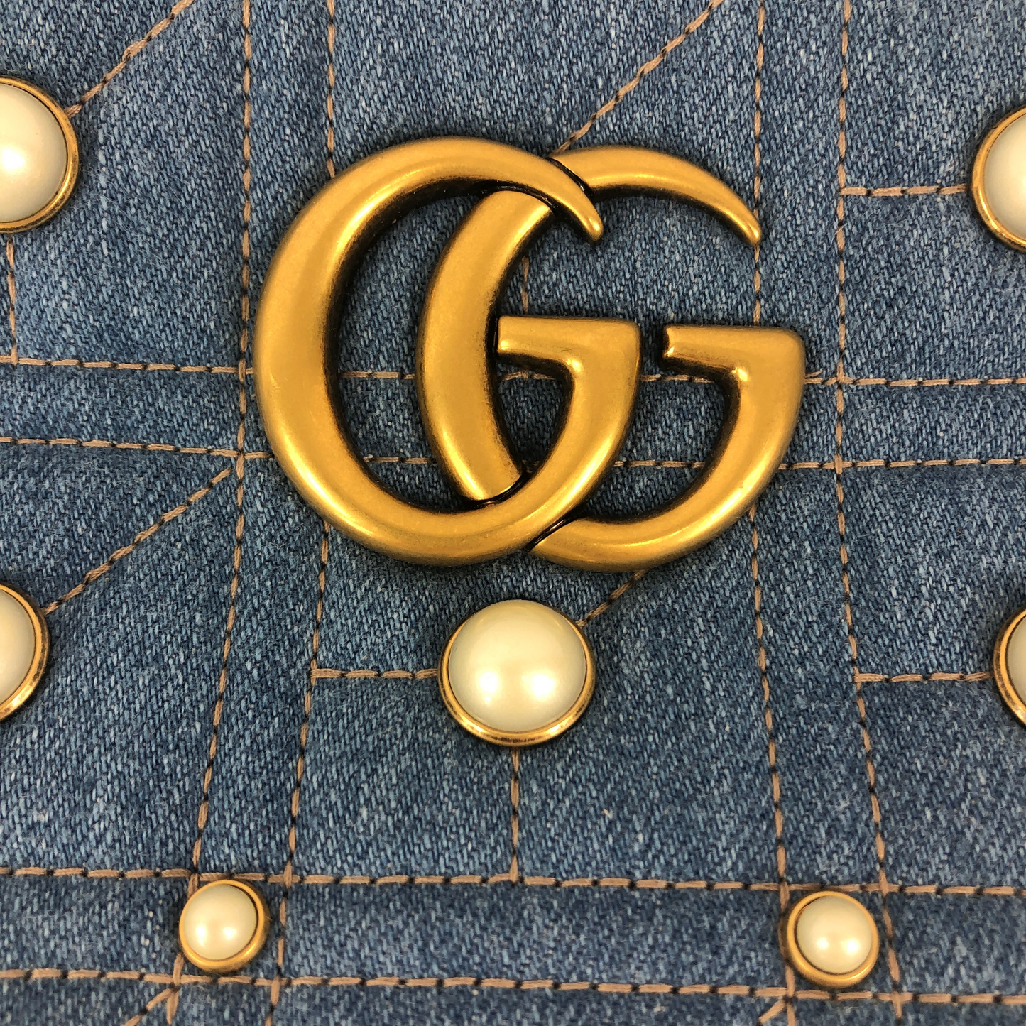 The Gucci Marmont Pearl Crossbody Bag in Denim is a modern take on a classic look. Light wash Matelassé denim Gucci Small GG Marmont Pearl Shoulder Bag with gold-tone hardware, single flat shoulder strap with chain-link accents, creme contrast stitching throughout, Running GG adornment at front face, pearl embellishments throughout exterior, coral satin interior lining, single interior slit pocket and zip closure at top. Includes dust bag. Authentic and rare handbags from Gavriel.us