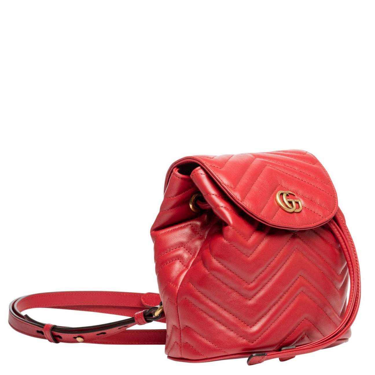 The Gucci Black Marmont Quilted Leather Backpack in Red features adjustable shoulder straps with post-stud fastening. Logo plaque at face. Fold over flap with magnetic tab fastening. Drawstring fastening at throat. Patch pocket and leather logo flag at interior. Leather lining in beige. Antiqued gold-tone hardware. Tonal stitching.