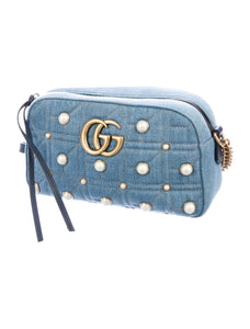The Gucci Marmont Pearl Crossbody Bag in Denim is a modern take on a classic look. Light wash Matelassé denim Gucci Small GG Marmont Pearl Shoulder Bag with gold-tone hardware, single flat shoulder strap with chain-link accents, creme contrast stitching throughout, Running GG adornment at front face, pearl embellishments throughout exterior, coral satin interior lining, single interior slit pocket and zip closure at top. Includes dust bag. Authentic and rare handbags from Gavriel.us