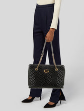 Load image into Gallery viewer, The Gucci GG Marmont Matelassé Leather Shoulder Bag in Black is a gorgeous leather bag with a tote silhouette which is accented by antique gold-tone hardware. Exquisite matelasse stitching accentuates the streamlined silhouette of a trim tote bag branded with antiqued double-G hardware inspired by an archival design.