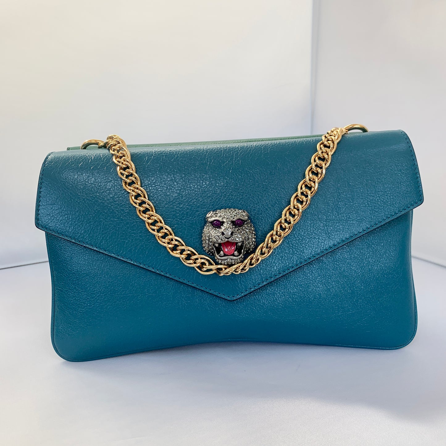 This is a two toned, double sided Gucci bag. The style is called Thiara and it looks like two envelopes back to back. One side is a mellow Robin blue. The other side is a jade green. The blue side has a jewel encrusted Raja tiger head on the magnetic clasp. The green side has the iconic double GG on the button clasp. There is a fixed Gucci gold short chain on the top and a strap is also included to make this a should bag or crossbody.