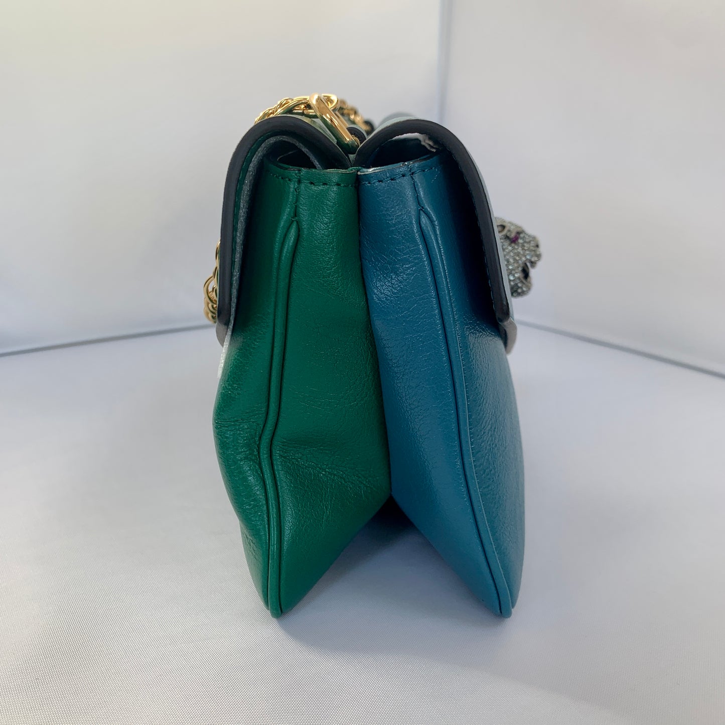 This is a two toned, double sided Gucci bag. The style is called Thiara and it looks like two envelopes back to back. One side is a mellow Robin blue. The other side is a jade green. The blue side has a jewel encrusted Raja tiger head on the magnetic clasp. The green side has the iconic double GG on the button clasp. There is a fixed Gucci gold short chain on the top and a strap is also included to make this a should bag or crossbody.