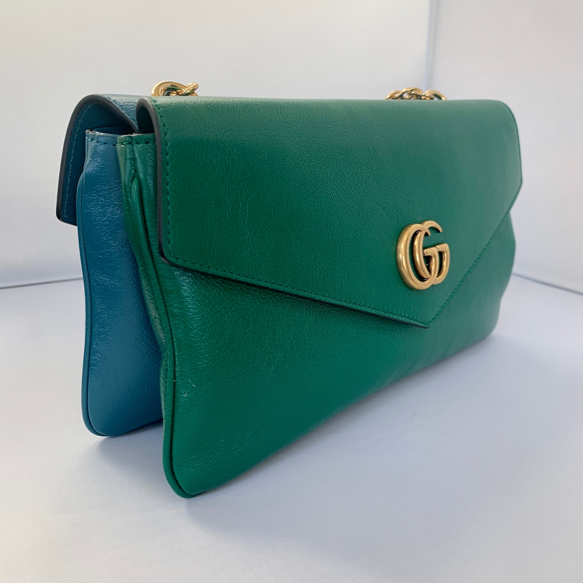 This is a two toned, double sided Gucci bag. The style is called Thiara and it looks like two envelopes back to back. One side is a mellow Robin blue. The other side is a jade green. The blue side has a jewel encrusted Raja tiger head on the magnetic clasp. The green side has the iconic double GG on the button clasp. There is a fixed Gucci gold short chain on the top and a strap is also included to make this a should bag or crossbody.