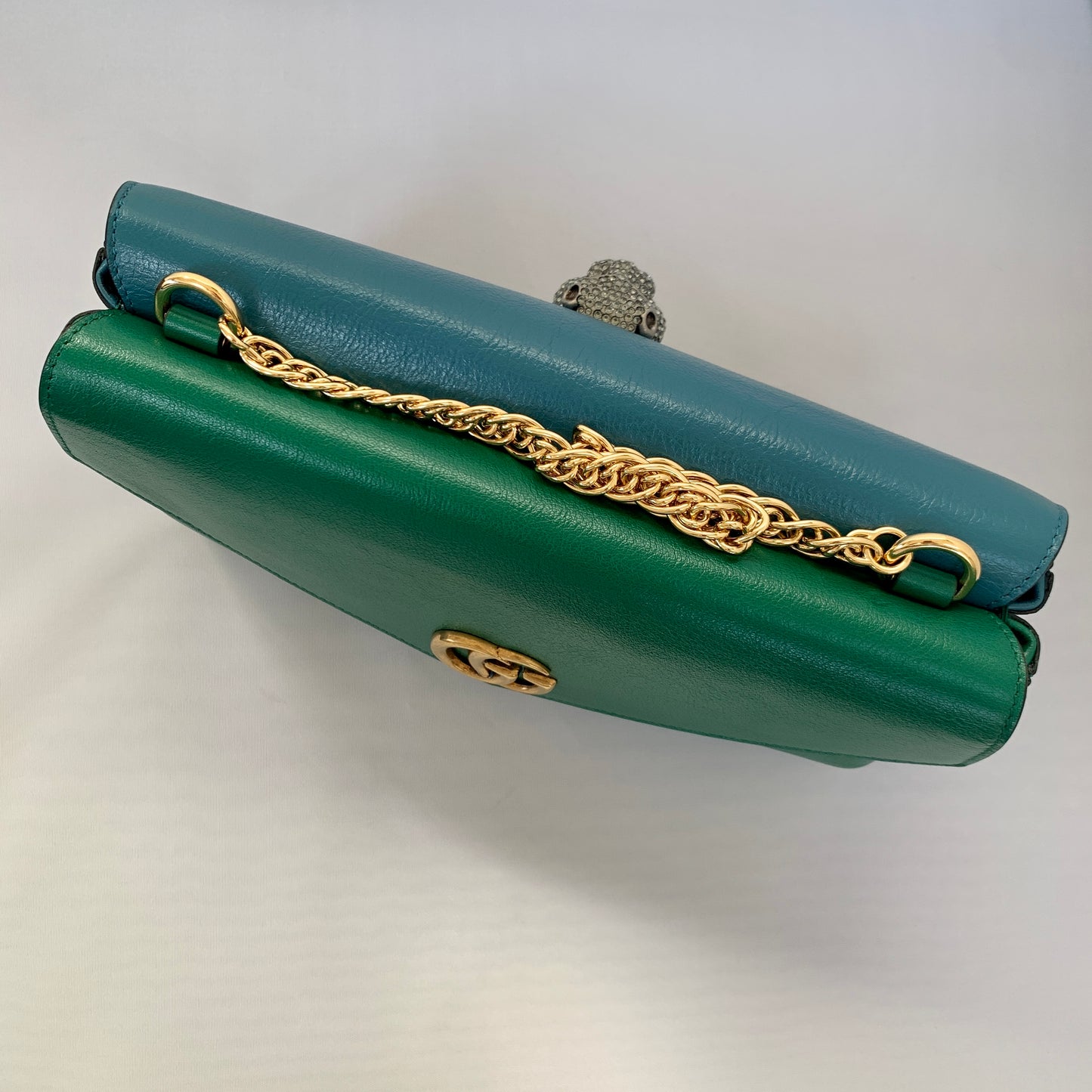 This is a two toned, double sided Gucci bag. The style is called Thiara and it looks like two envelopes back to back. One side is a mellow Robin blue. The other side is a jade green. The blue side has a jewel encrusted Raja tiger head on the magnetic clasp. The green side has the iconic double GG on the button clasp. There is a fixed Gucci gold short chain on the top and a strap is also included to make this a should bag or crossbody.