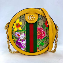 Load image into Gallery viewer, Brighten up your wardrobe with the Gucci mini Ophidia GG Flora round crossbody in a sunny yellow. A slim, rounded silhouette is crafted from GG supreme canvas and pebbled leather to create this fun and unique bag. This accessory is covered in a multicolor flora print that is accented by mustard yellow trim and a signature red and green web. 
