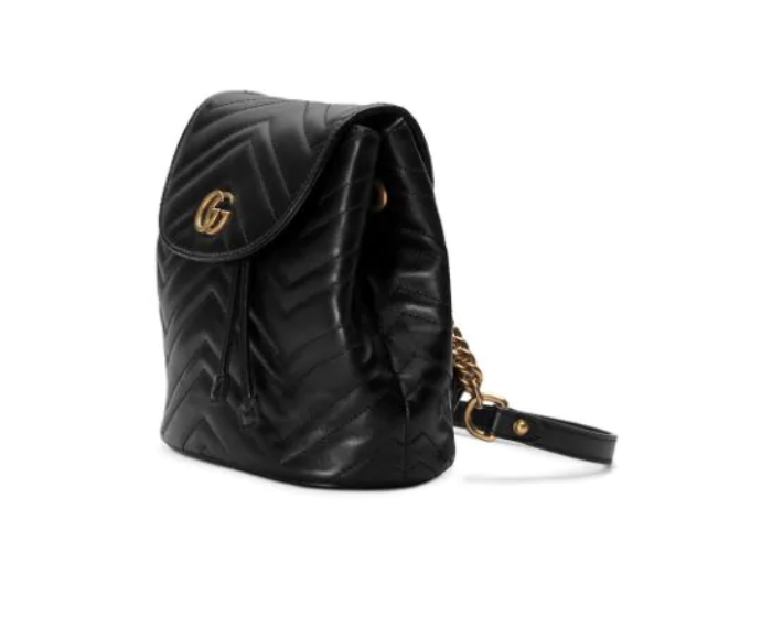 The Gucci Black Marmont Quilted Leather Backpack features adjustable shoulder straps with post-stud fastening. Logo plaque at face. Fold over flap with magnetic tab fastening. Drawstring fastening at throat. Patch pocket and leather logo flag at interior. Leather lining in beige. Antiqued gold-tone hardware. Tonal stitching.