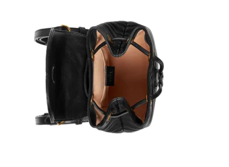 The Gucci Black Marmont Quilted Leather Backpack features adjustable shoulder straps with post-stud fastening. Logo plaque at face. Fold over flap with magnetic tab fastening. Drawstring fastening at throat. Patch pocket and leather logo flag at interior. Leather lining in beige. Antiqued gold-tone hardware. Tonal stitching.