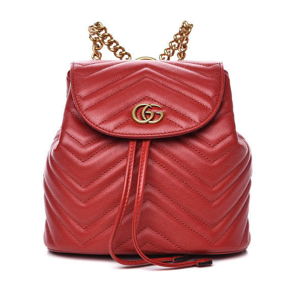 The Gucci Black Marmont Quilted Leather Backpack in Red features adjustable shoulder straps with post-stud fastening. Logo plaque at face. Fold over flap with magnetic tab fastening. Drawstring fastening at throat. Patch pocket and leather logo flag at interior. Leather lining in beige. Antiqued gold-tone hardware. Tonal stitching.
