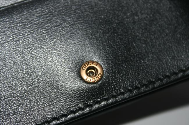 The Gucci GG Marmont Web Quilted Card Case Wallet in Black is a mini snap wallet in quilted black leather. A Double GG logo adorns the front along with a signature Gucci web. The snap closure opens to 4 card slots, a slip pocket, a bill slot with floral linen lining, and a zipped compartment. 
