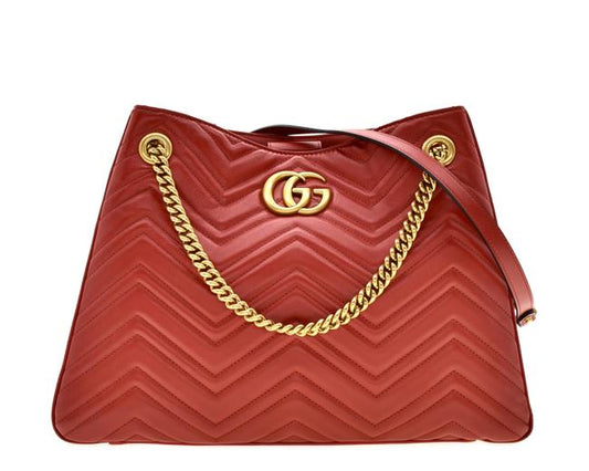 The Gucci GG Marmont Apollo Chevron Tote Shoulder Bag in Red is a unique piece that features the chevron, zig zag patterned stitching in a smooth calfskin red leather. The curved silhouette hangs from two chain shoulder straps with leather pads, while a GG logo in gold-tone hardware sits on the front and a stitched GG is on the back. 