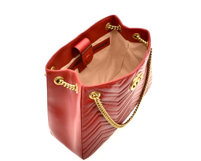 The Gucci GG Marmont Apollo Chevron Tote Shoulder Bag in Red is a unique piece that features the chevron, zig zag patterned stitching in a smooth calfskin red leather. The curved silhouette hangs from two chain shoulder straps with leather pads, while a GG logo in gold-tone hardware sits on the front and a stitched GG is on the back. 