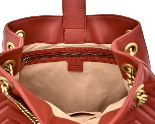 The Gucci GG Marmont Apollo Chevron Tote Shoulder Bag in Red is a unique piece that features the chevron, zig zag patterned stitching in a smooth calfskin red leather. The curved silhouette hangs from two chain shoulder straps with leather pads, while a GG logo in gold-tone hardware sits on the front and a stitched GG is on the back. 