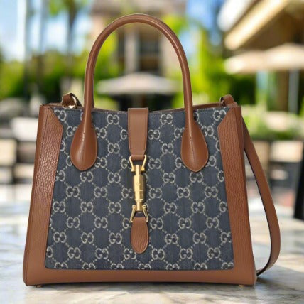 Gucci Jackie bag in Denim.  Medium Tote with removable crossbody strap in a vaccia brown.  Front gold clip.  Brown leather trim.  Interlocking GG logo in blue denim.